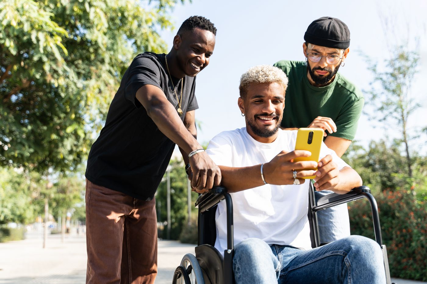Three friends smiling at a phone together, one of them in a wheelchair
