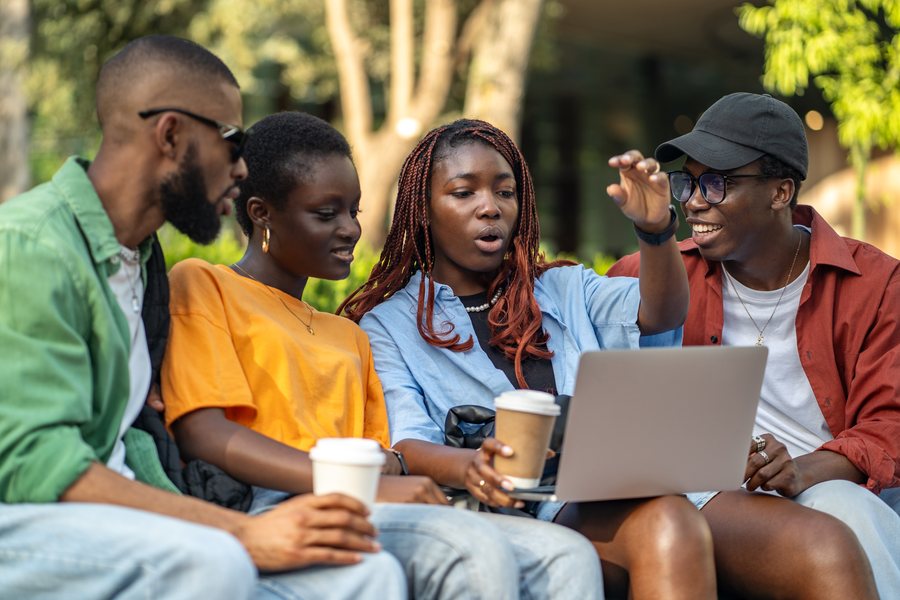 Four students outdoors looking at a laptop screen together